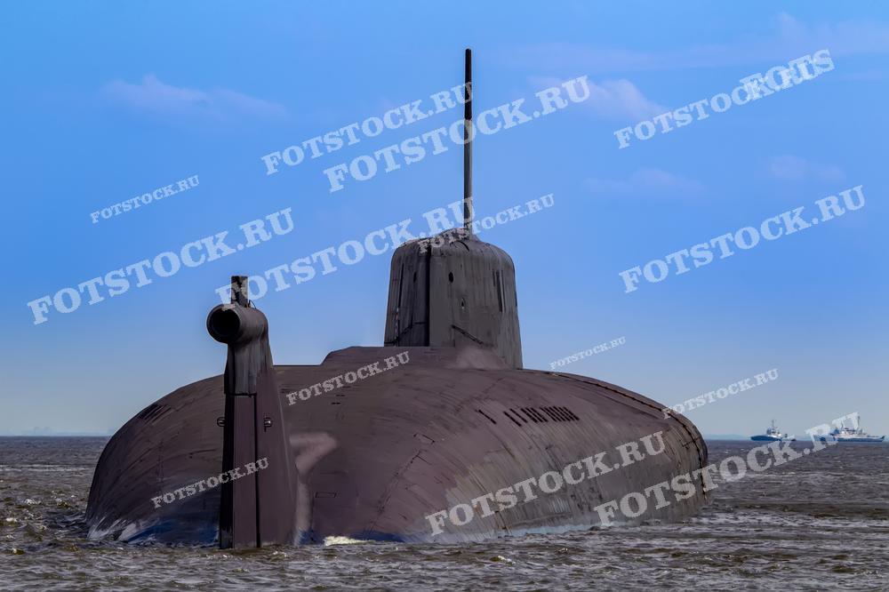 Фотография подводной лодки, движущейся по поверхности в открытом море, снятая с кормы. Силуэт судна на фоне голубого неба подчеркивает его мощь и оборонительные возможности военно-морского флота.